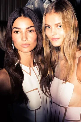 Two models with long, wavy hair showcasing refined styles in light dresses at Carolina Herrera SS16.