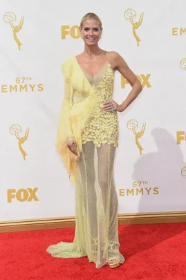 Person on red carpet in a sheer yellow gown with floral details at the 67th Emmy Awards.