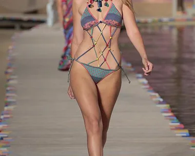 Model walks runway in colorful bikini and hat at Tommy Hilfiger fashion show.