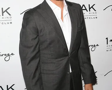 A man in a suit stands against a backdrop with text "1 OAK" and "Mirage."