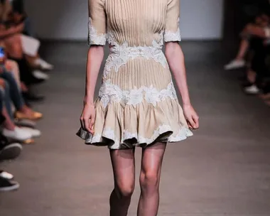 Model on runway wearing a cream pleated dress with lace details and ruffled hem from Zimmermann SS16 collection.