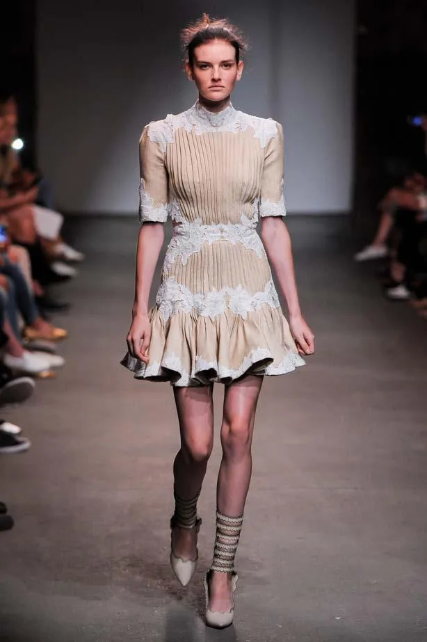 Model on runway wearing a cream pleated dress with lace details and ruffled hem from Zimmermann SS16 collection.