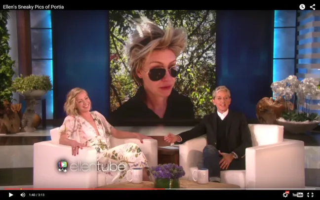 Screenshot from "Ellen's Sneaky Pics of Portia" shows Ellen and her guest laughing at a large photo of Portia with messy hair and sunglasses.