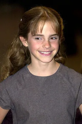 Young girl with long brown hair smiling, wearing a gray dress, pictured in a candid moment.