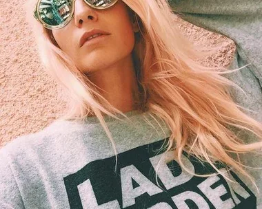 A woman with long blonde hair wearing sunglasses and a grey sweatshirt that says "LADY GARDEN."