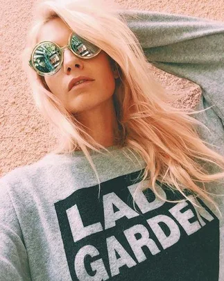 A woman with long blonde hair wearing sunglasses and a grey sweatshirt that says "LADY GARDEN."