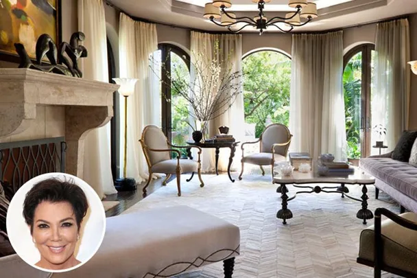 Elegant living room with arched windows, neutral decor, and a large chandelier. Inset of a woman's face in the bottom left.