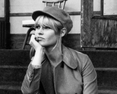 Black and white photo of a woman in a cap and coat sitting on steps, looking thoughtful.