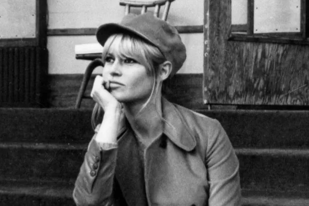 Black and white photo of a woman in a cap and coat sitting on steps, looking thoughtful.