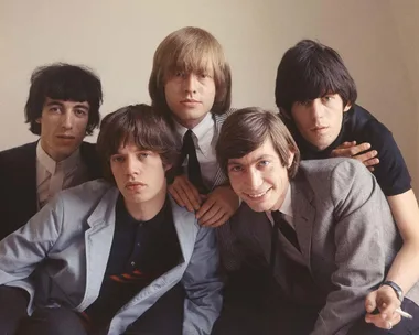 A classic band from the 60s posing together, dressed in suits with varying expressions, against a plain background.