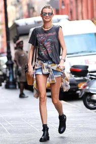 Woman in Iron Maiden shirt, denim shorts, boots; flannel tied at waist, walking on street.