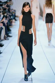 Model walking down runway in a black, high-neck dress with side straps and thigh-high slit.