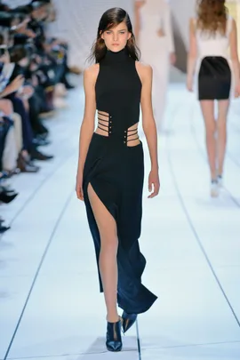 Model walking down runway in a black, high-neck dress with side straps and thigh-high slit.