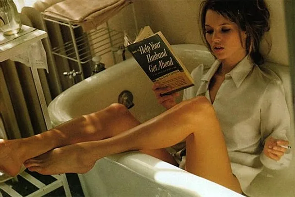 A woman in a bathtub reading "Help Your Husband Get Ahead" while smoking.