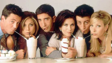 The six main characters from Friends sipping milkshakes, all leaning in towards the counter with playful expressions.