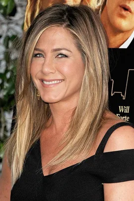 A woman with straight blonde hair and an off-shoulder black dress smiles at a red carpet event.