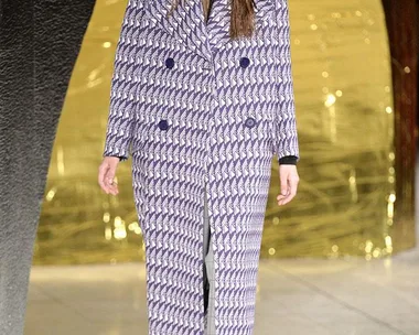 A model in a patterned purple coat and lace-up boots walks the runway at the Miu Miu SS16 fashion show.