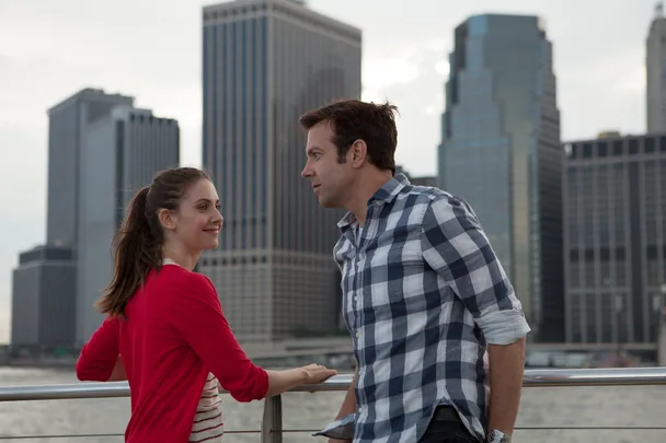 Alison Brie and Jason Sudeikis in a scene from the film "Sleeping with Other People," standing by a waterfront with city skyscrapers.