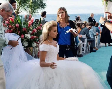 Behind the scenes of "The Godfather," crew adjusts costume on actress in a wedding dress by the ocean.