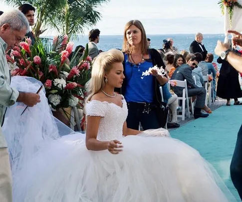 Behind the scenes of "The Godfather," crew adjusts costume on actress in a wedding dress by the ocean.