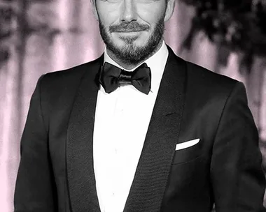 "Man in a tuxedo with styled hair and beard, smiling at an event."