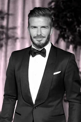 "Man in a tuxedo with styled hair and beard, smiling at an event."