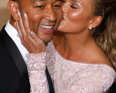 A woman in a pink dress kisses a man in a suit on the cheek, both smiling.