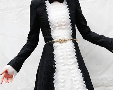 Person wearing a black and white textured dress with a geometric pattern, accessorized with a gold belt.