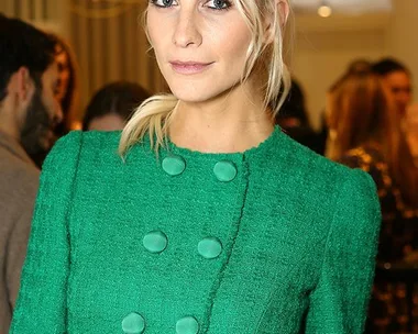 Poppy Delevingne in a green buttoned dress, posing at a party with people in the background.