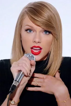 Woman with blonde hair and red lipstick singing into a microphone, hand on chest, wearing a black top.