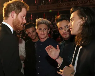 Prince Harry meets members of One Direction at a formal event, standing in a circle and conversing animatedly.