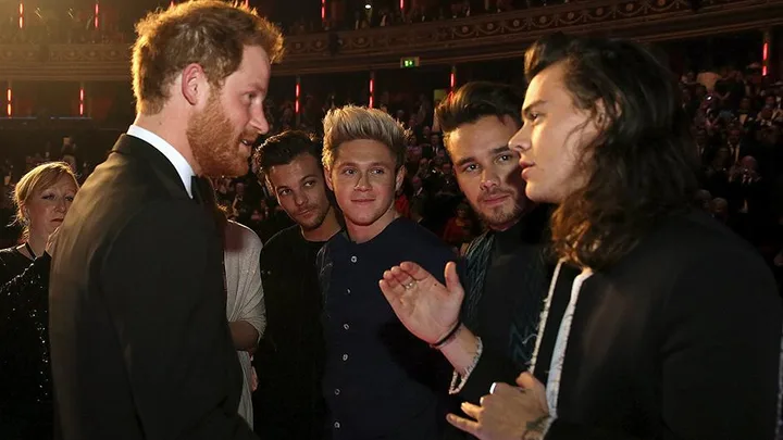 Prince Harry meets members of One Direction at a formal event, standing in a circle and conversing animatedly.