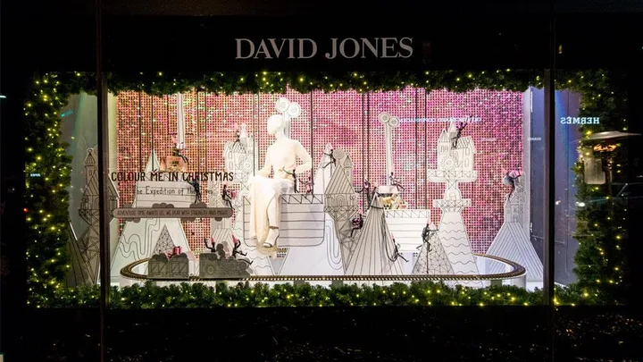 David Jones Christmas window display featuring a mannequin, festive decorations, and a miniature Christmas village with lights and greenery.