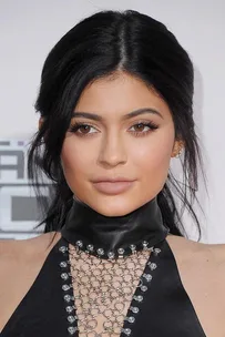 Woman with long dark hair, wearing a black leather and chain-link dress at a public event.