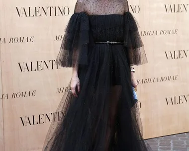 Woman in a sheer black Valentino gown at a fashion event, standing against a branded backdrop.