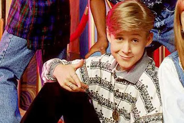 Young actor sitting with a smile, wearing a patterned shirt; part of a group photo in a teen drama scene.