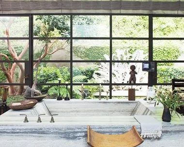 Spacious bathroom with a large stone tub, plants, and garden view through expansive windows.