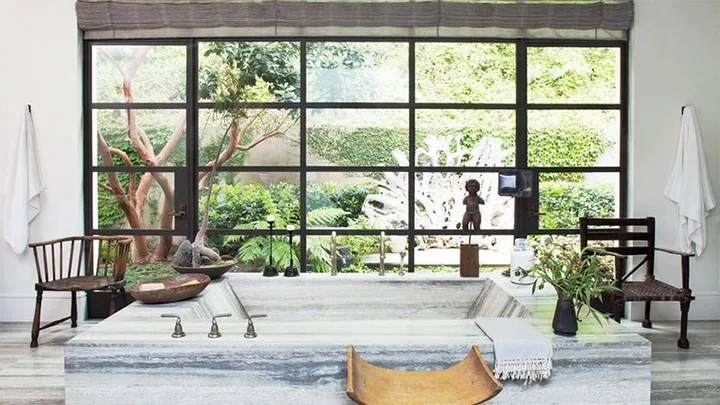 Spacious bathroom with a large stone tub, plants, and garden view through expansive windows.