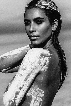 Black-and-white image of a woman with wet hair, partially covered in white paint, posing in a desert setting.