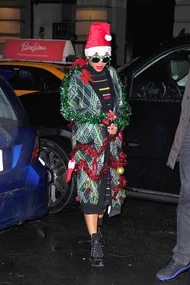 Person in festive plaid sweater, Santa hat, and Christmas decorations, standing by cars at night.