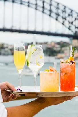 Four elegant summer cocktails on a tray with the Sydney Harbour Bridge in the background.