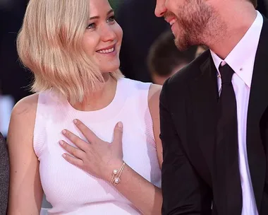 Jennifer Lawrence and Liam Hemsworth smiling at each other at an event, with Jennifer's hand on her chest.