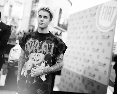 A person with tattoos in a Nirvana shirt stands in front of a Fiat backdrop at an event.