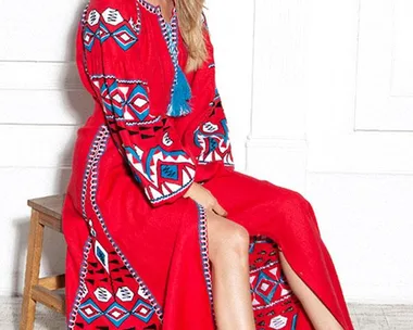 Woman in a red, patterned dress with blue accents, sitting on a stool, wearing white sneakers.