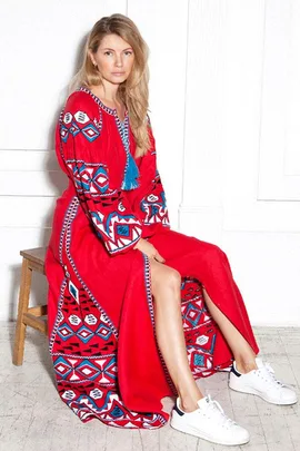 Woman in a red, patterned dress with blue accents, sitting on a stool, wearing white sneakers.