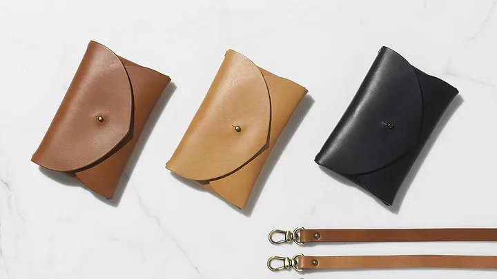 Three leather clutch bags in brown, tan, and black, featuring snap closures and two detachable leather straps with metal clasps.