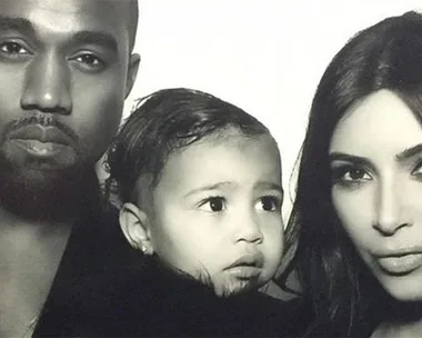 Black-and-white photo featuring two adults and a child between them, all looking towards the camera with neutral expressions.