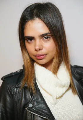 Portrait of a woman with brown hair wearing a black leather jacket and white sweater, looking directly at the camera.