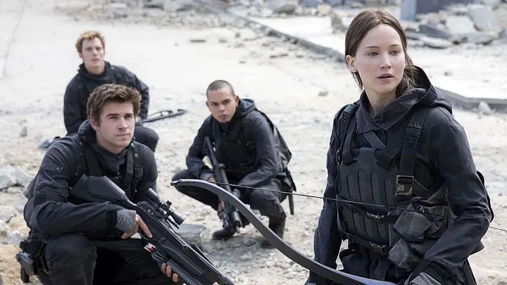 "Katniss Everdeen with a bow and three armed soldiers in a post-apocalyptic setting from The Hunger Games series."