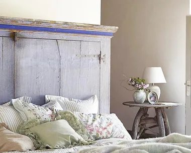 Rustic bedroom with a wooden headboard, floral bedding, and a side table with a lamp and vase. Cozy and inviting atmosphere.